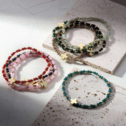 Assorted crystal stretch bracelets with gold cross charm in multiple colorways
