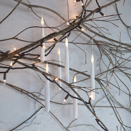 Set of 6 white hanging LED flameless candles suspended from bare branches with string lights