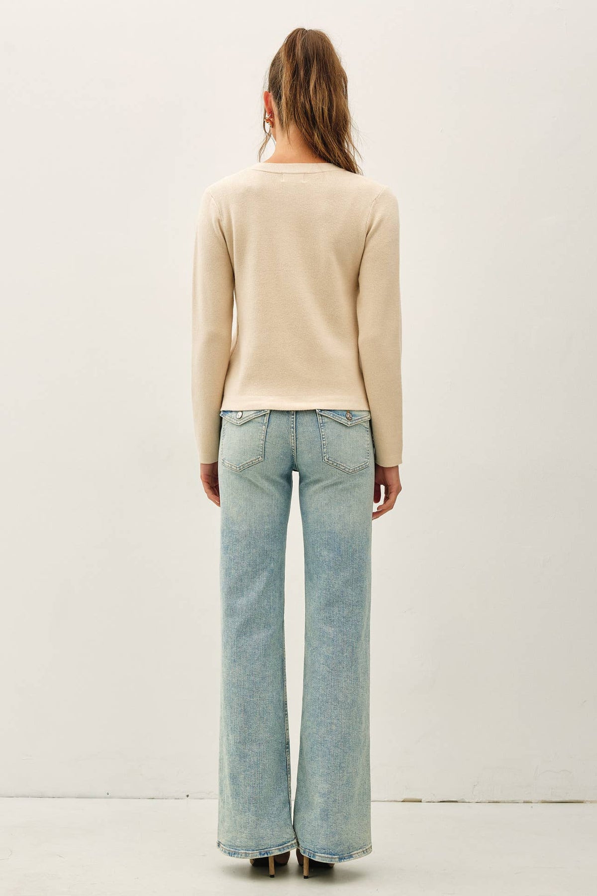 Beige long-sleeve crewneck cardigan with snap button closure, styled with wide-leg jeans