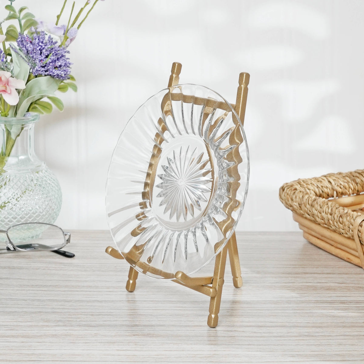 Gold satin metal easel displaying a clear cut-glass plate on a wooden surface