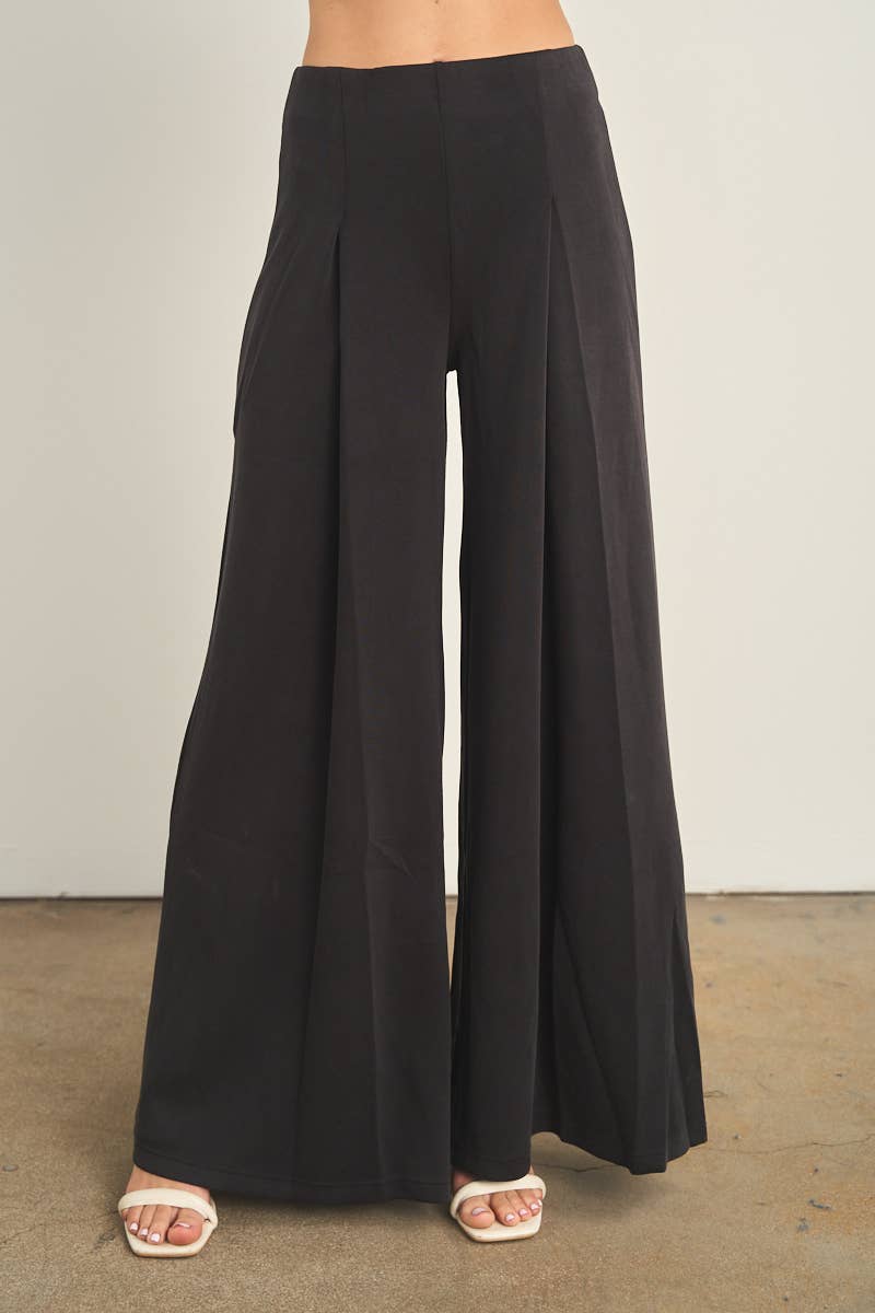 Black wide-leg palazzo pants with pleats, high waist, worn with white heeled sandals