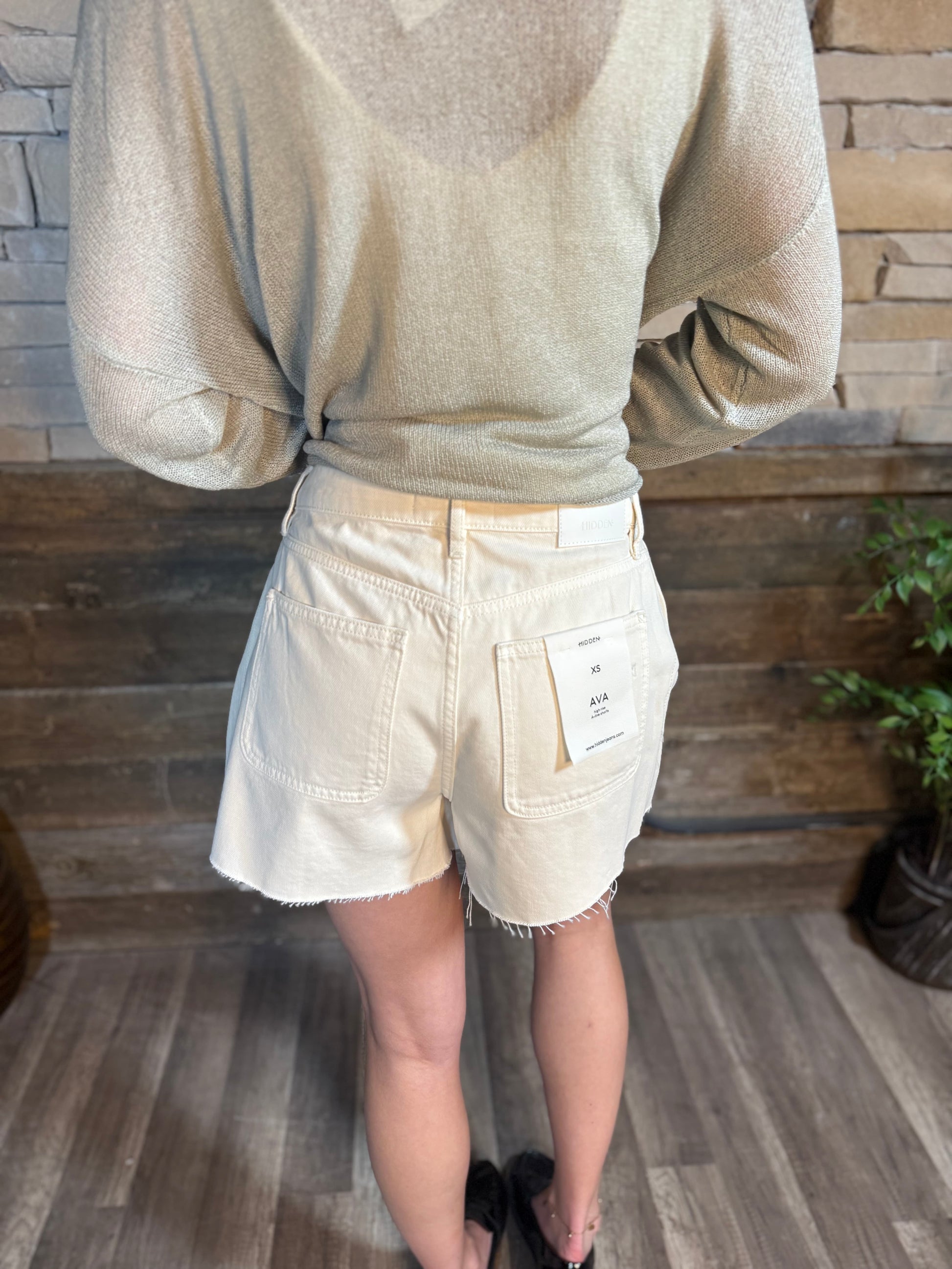Back view of ecru denim cutoff shorts with patch pockets and raw hem