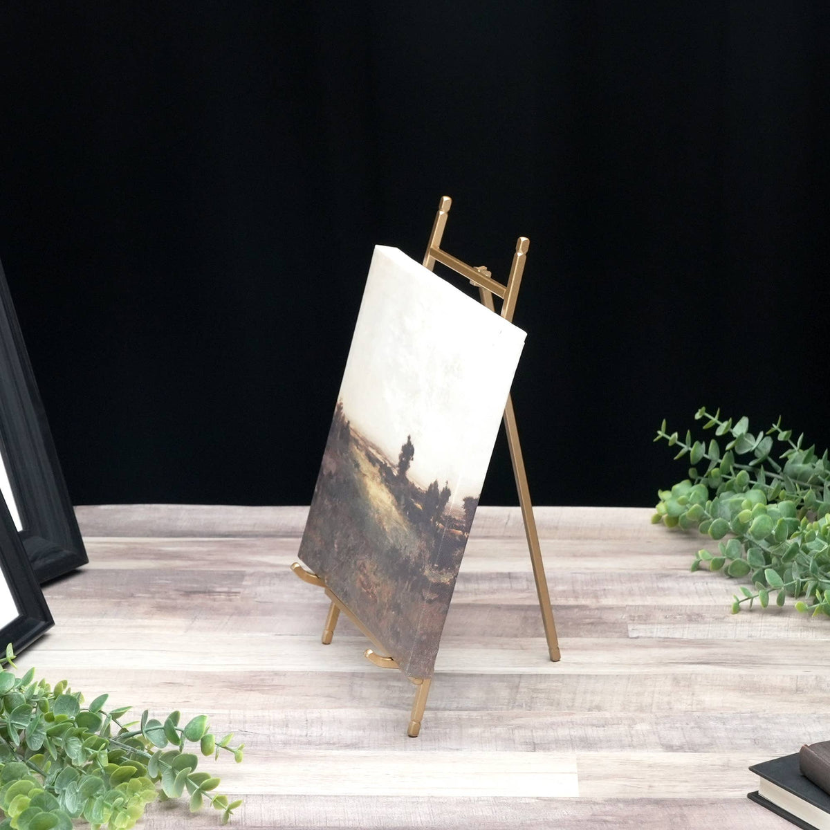 Gold satin metal tabletop easel holding a small landscape canvas painting