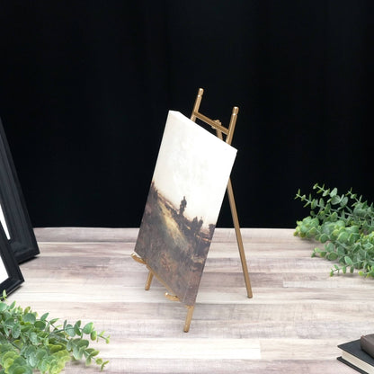 Gold satin metal tabletop easel holding a small landscape canvas painting