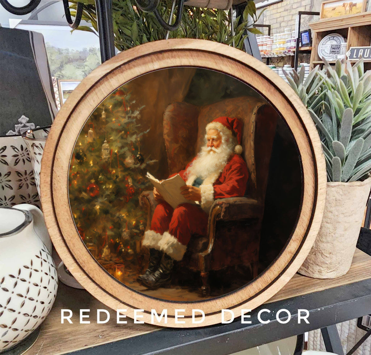 Round wood-framed canvas art of Santa reading by a decorated Christmas tree