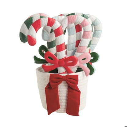 Decorative candy cane ornaments with colorful bows arranged in a white rope basket with red ribbon