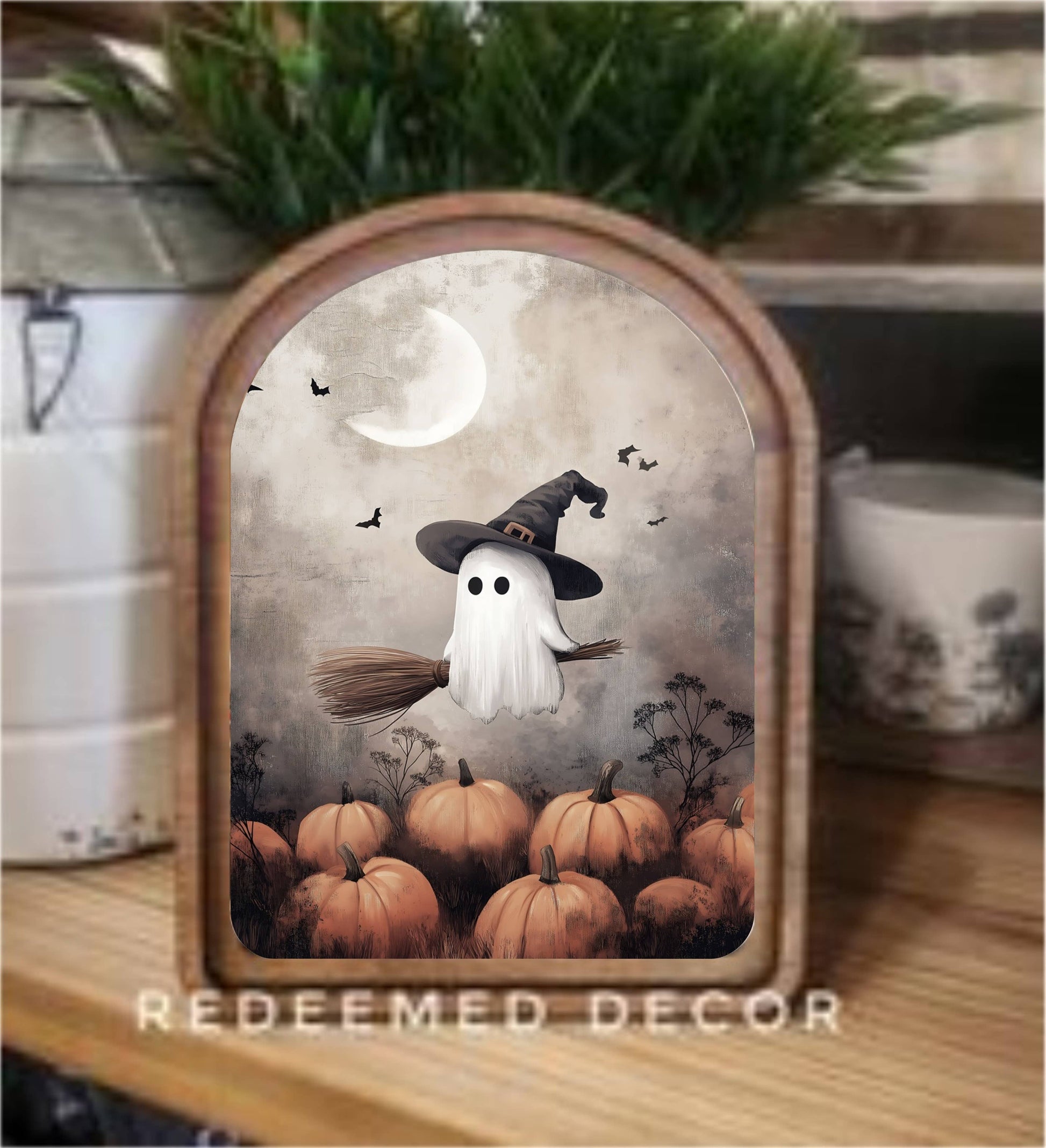 Arched wood framed canvas art featuring ghost witch riding broom over pumpkins under moon