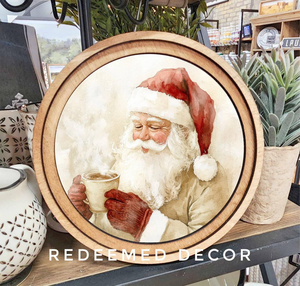 Round wood-framed canvas art featuring watercolor Santa Claus holding steaming cocoa mug