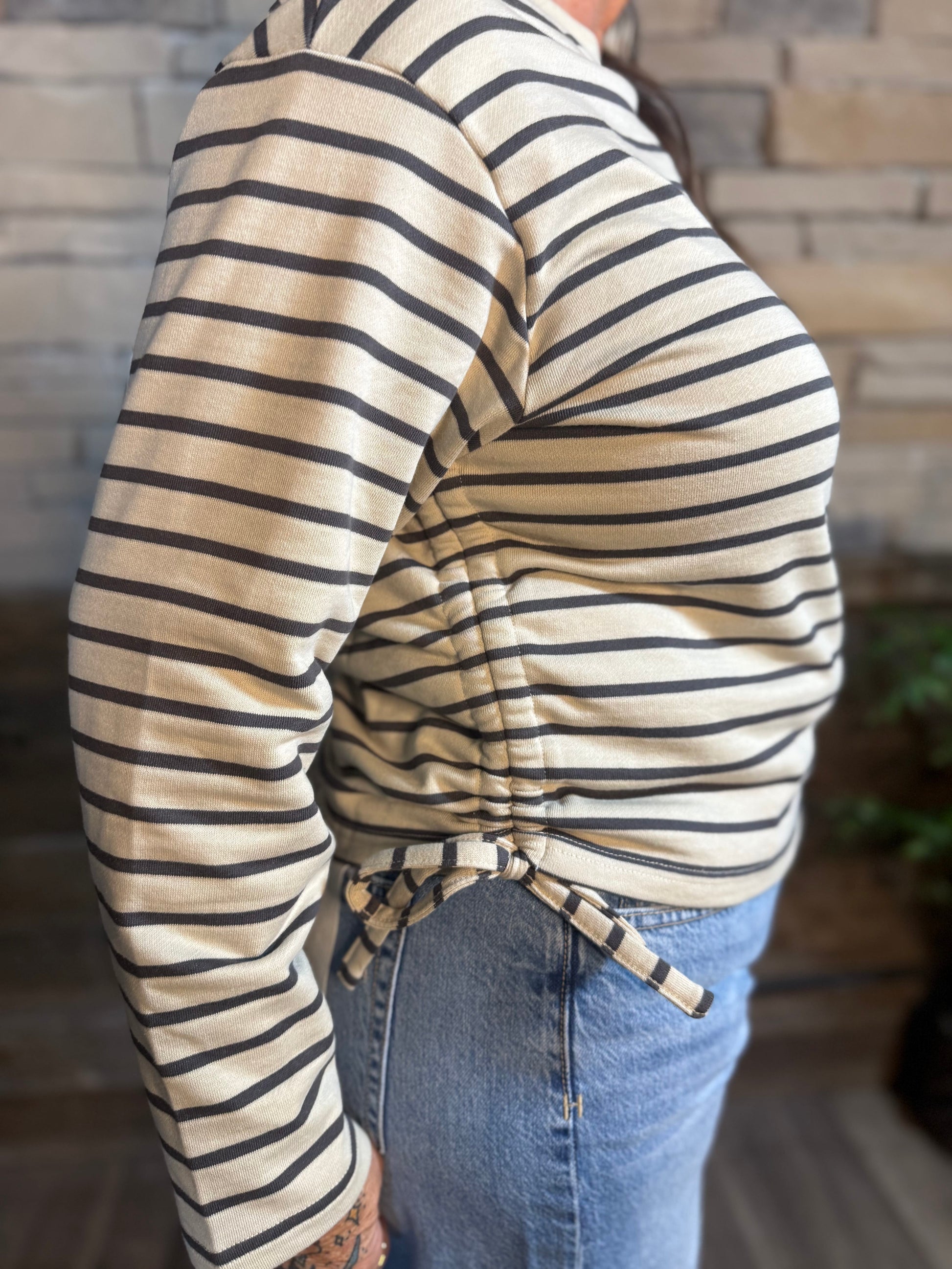 Beige striped crewneck sweatshirt with side drawstring detail, worn with blue jeans