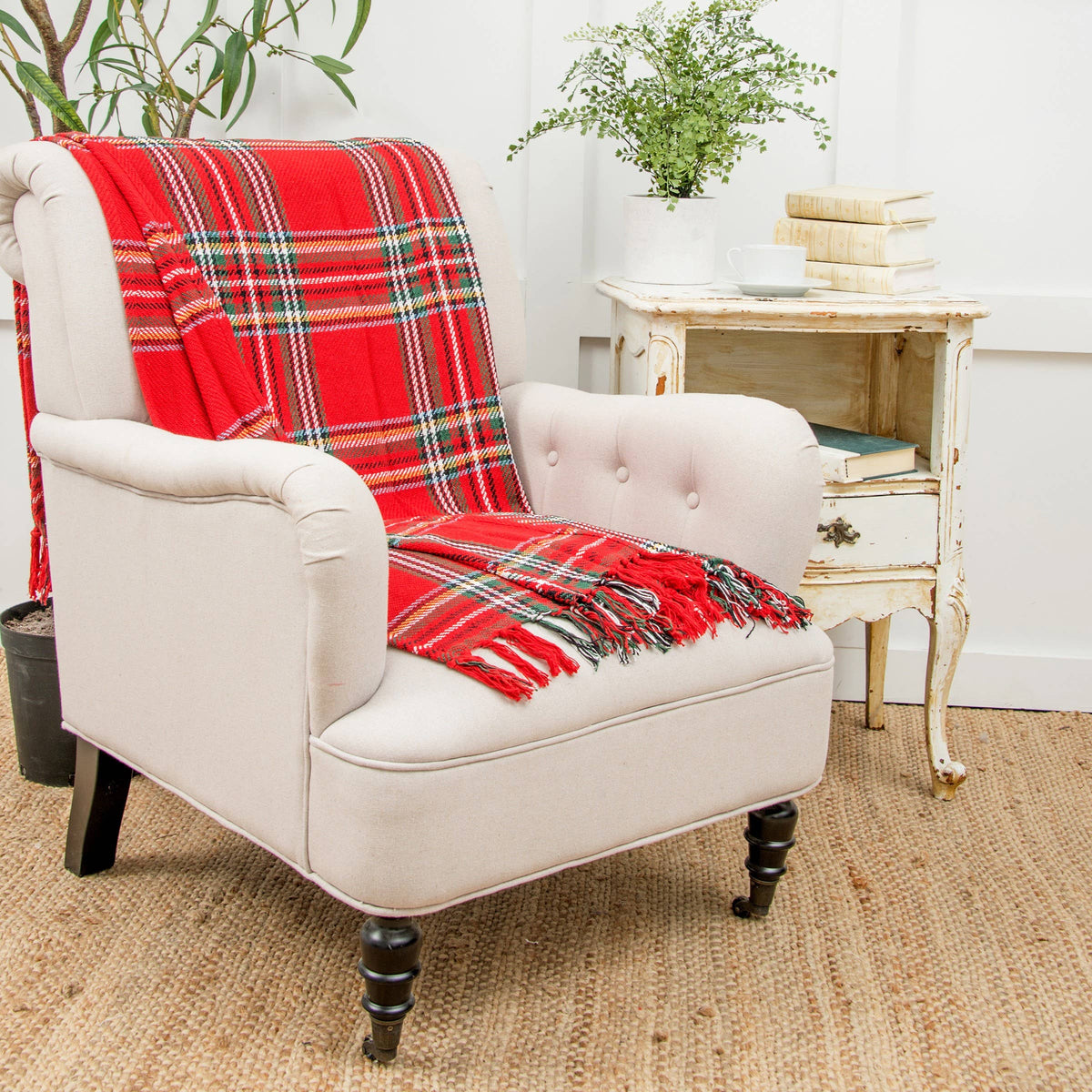 Red tartan plaid throw blanket with fringe draped over a cream tufted armchair