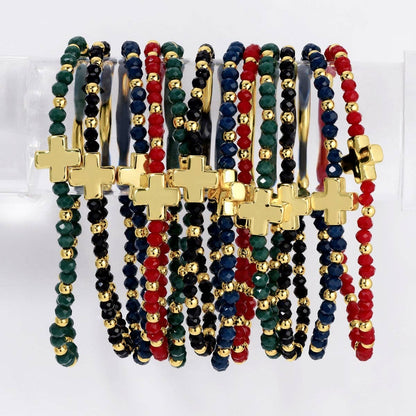 Assorted gold cross stretch bracelets with red, black, navy, and green crystal beads on display stand