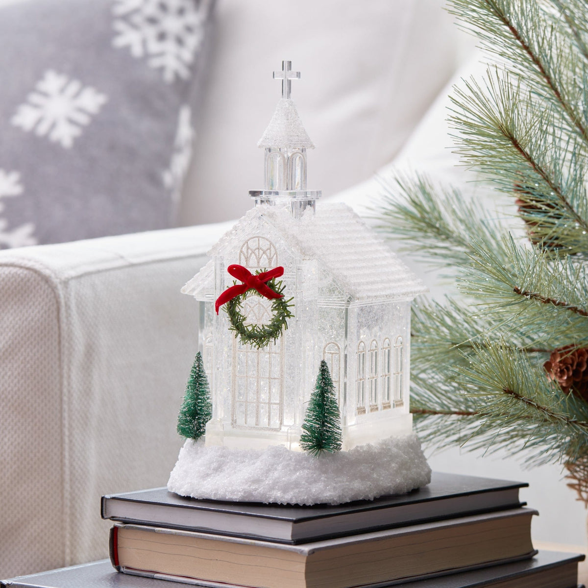 Illuminated clear acrylic church snow globe with wreath, miniature trees, and cross steeple on books
