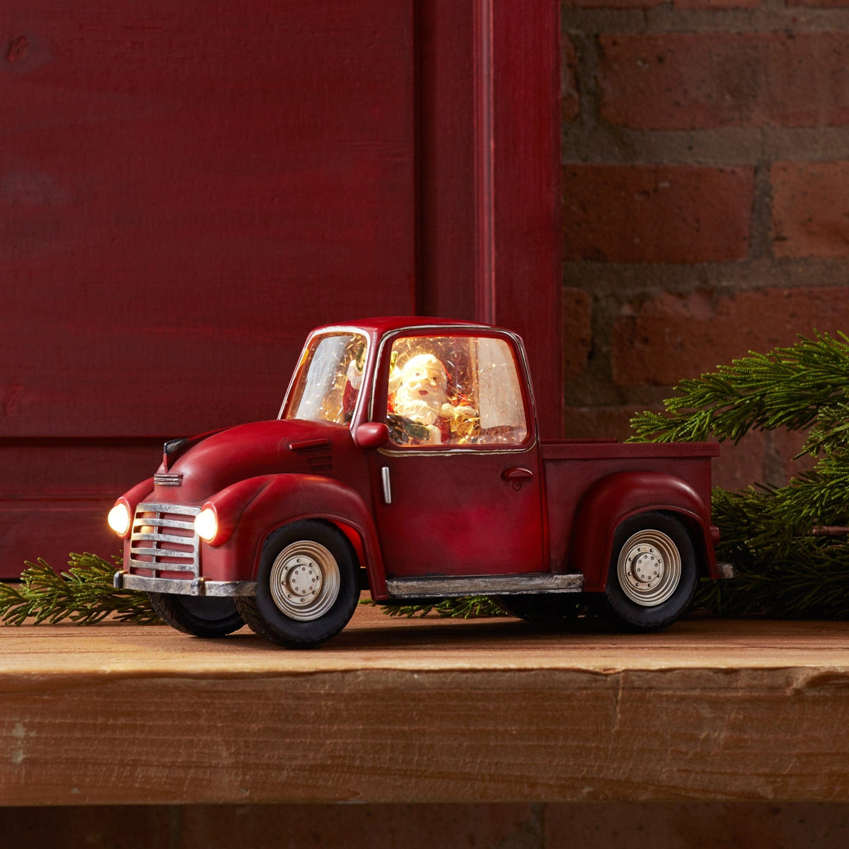 Vintage-style red pickup truck decoration with illuminated headlights and Santa figurine inside cab