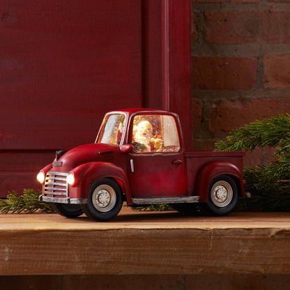 Vintage-style red pickup truck decoration with illuminated headlights and Santa figurine inside cab