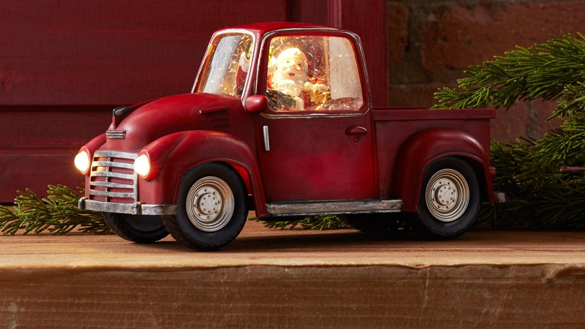 Vintage-style red pickup truck figurine with glowing headlights and illuminated Santa inside cab