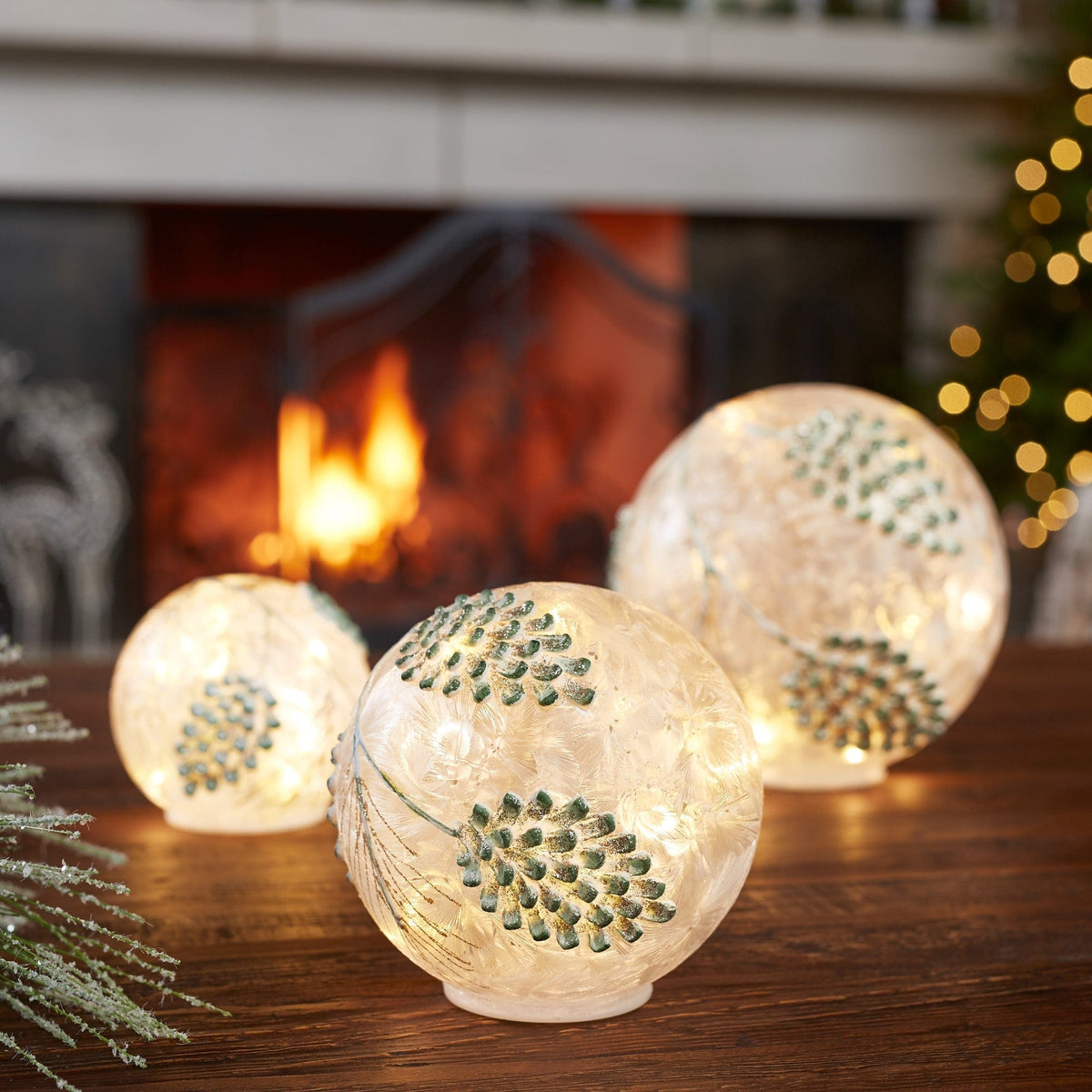 Three illuminated crackle glass globes with green pine cone designs, glowing warmly on wooden surface