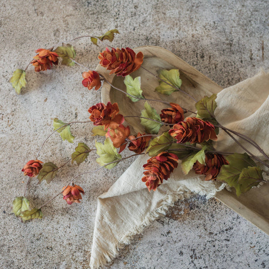 Artificial sienna hops stem with orange red blooms and green leaves on wood tray