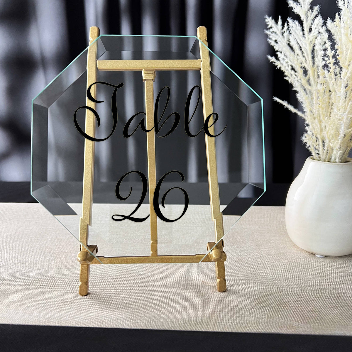 Gold satin metal easel holding clear octagonal acrylic table number sign on linen surface