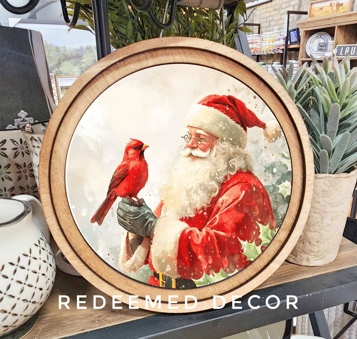Round wood-framed canvas art featuring Santa Claus holding a red cardinal bird