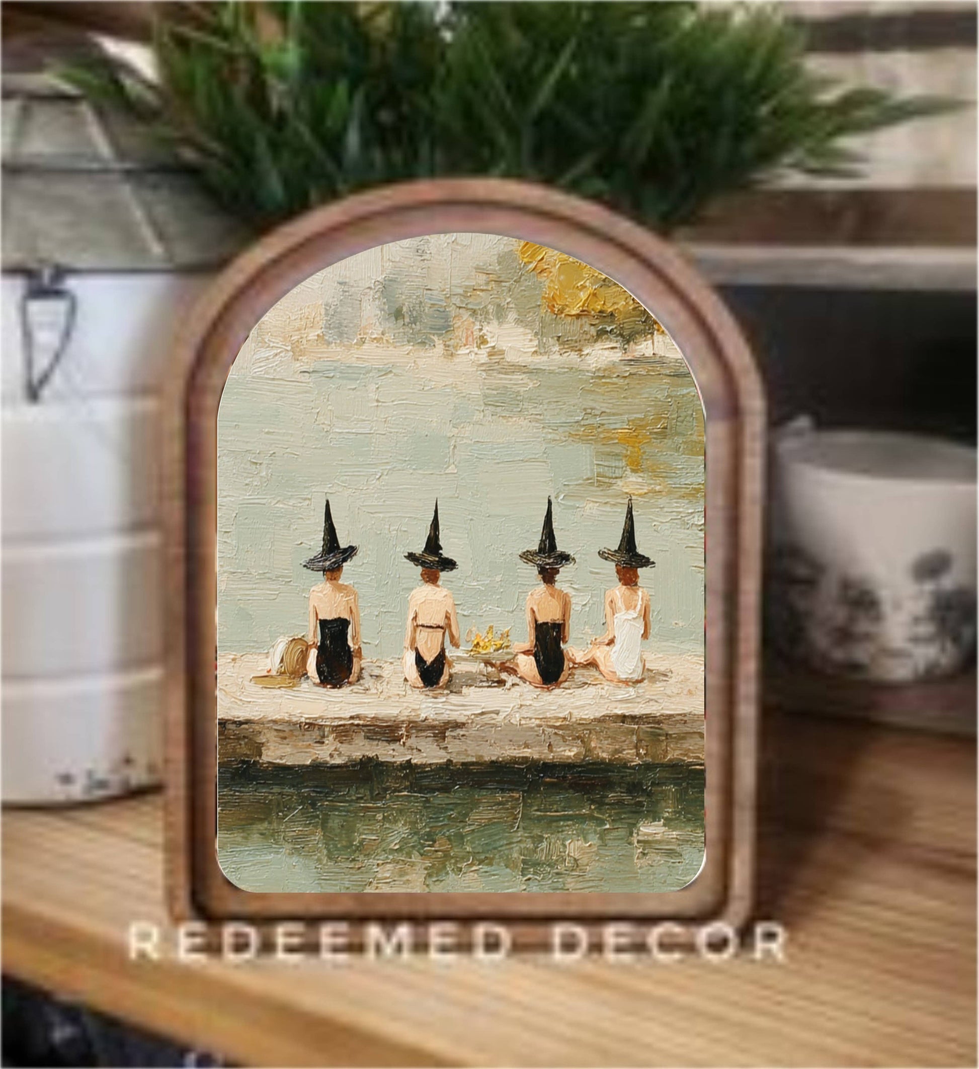 Arched wood-framed art print of four witches sitting by a lake in swimsuits