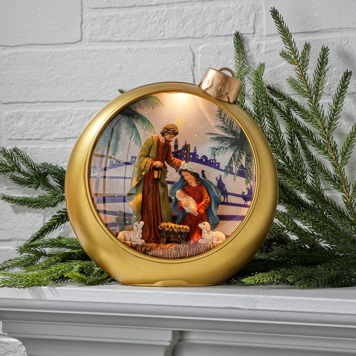 Gold ornament-shaped globe with lit Holy Family nativity scene inside, displayed on mantel