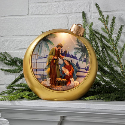 Gold ornament-shaped globe with lit Holy Family nativity scene inside, displayed on mantel