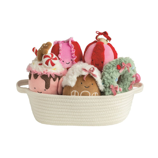 Five holiday-themed plush toys in a white rope basket, including gingerbread, wreath, and cupcake designs