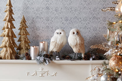 Pair of decorative white foam owl figurines on a holiday mantle with candles and pinecones