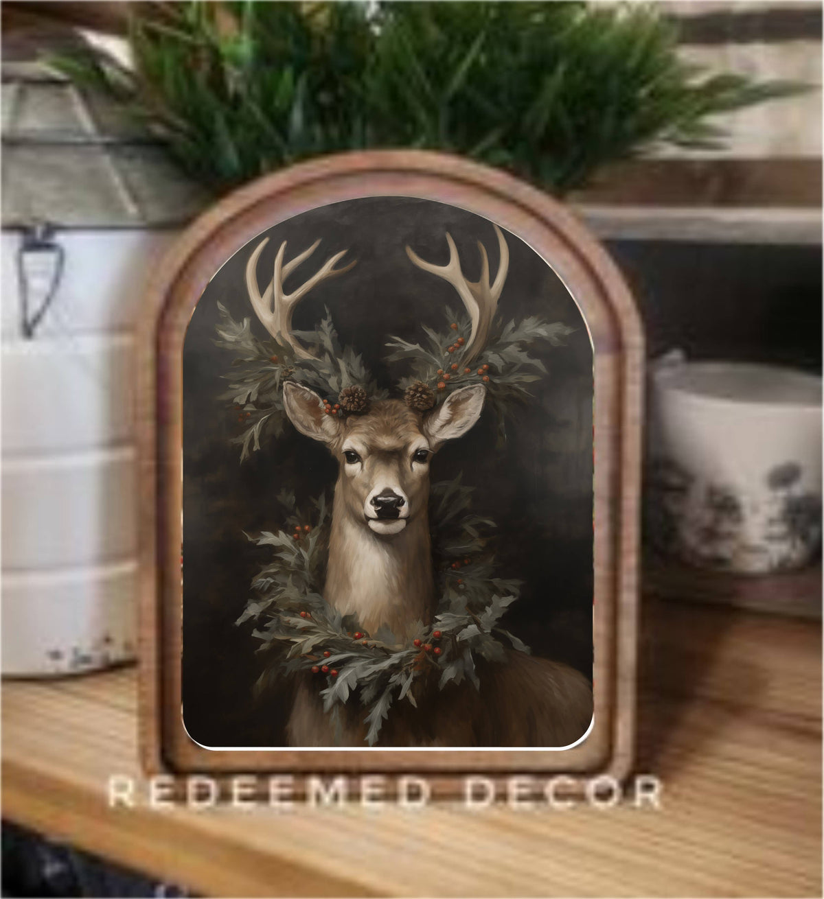 Arched wood-framed canvas art of a deer with antlers and holiday greenery wreath