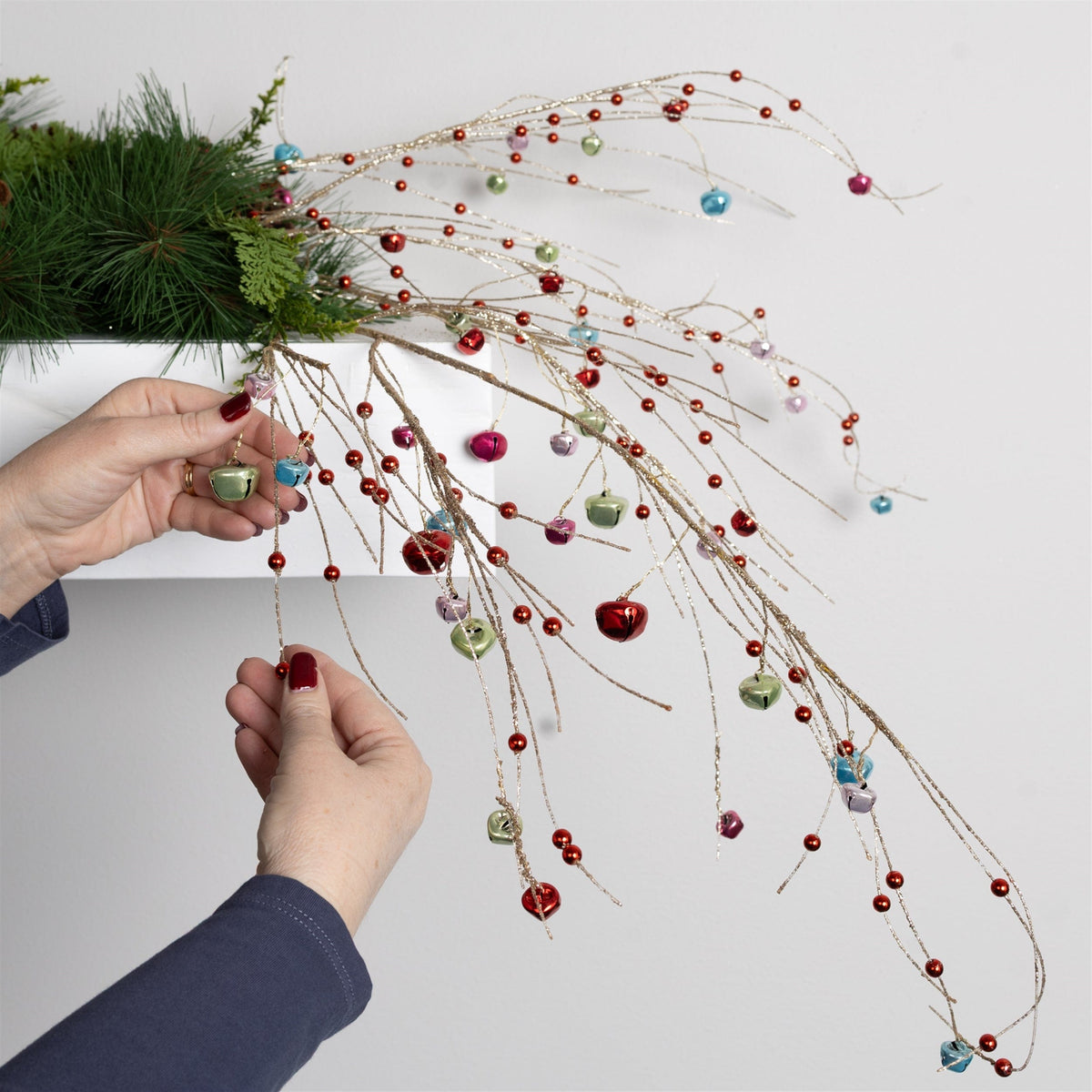 Hands arranging a decorative spray with multicolor jingle bells and beads on glitter branches