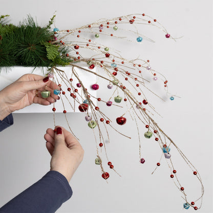 Hands arranging a decorative spray with multicolor jingle bells and beads on glitter branches