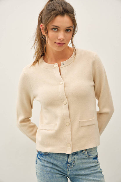 Cream cropped crewneck cardigan with snap buttons and front patch pockets