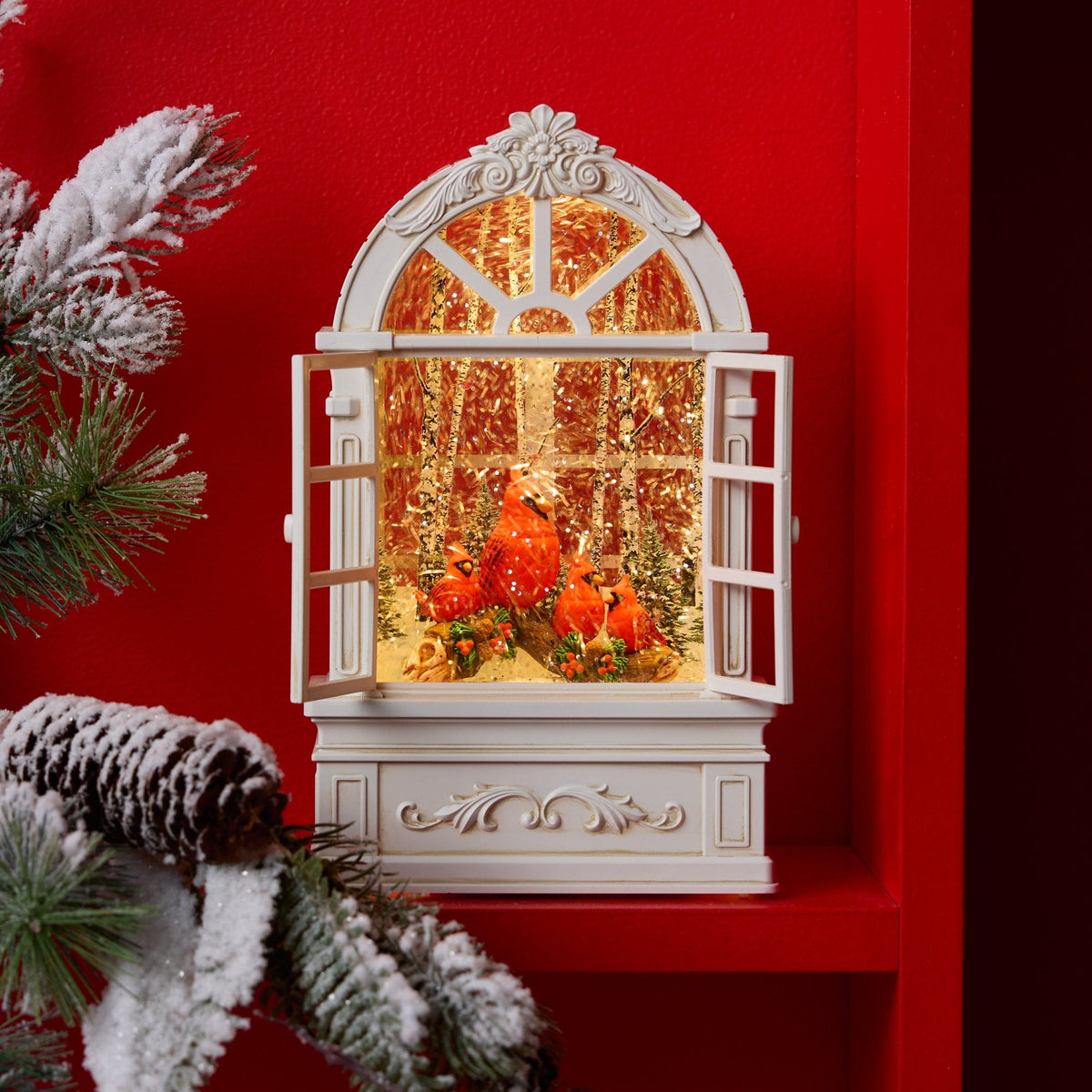 Illuminated window-shaped snow globe with red cardinal birds inside, white ornate frame