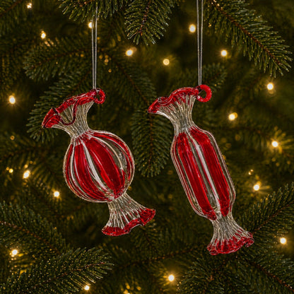 Two glass candy-shaped Christmas ornaments with red and clear striped details hanging on a tree