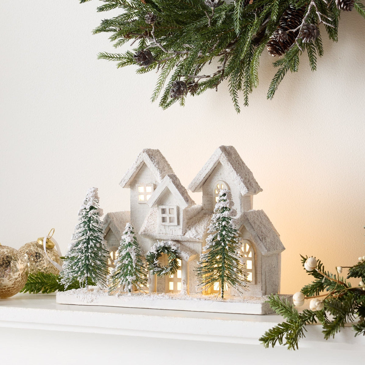 Snow-dusted white wooden village houses with warm LED lights and miniature green trees