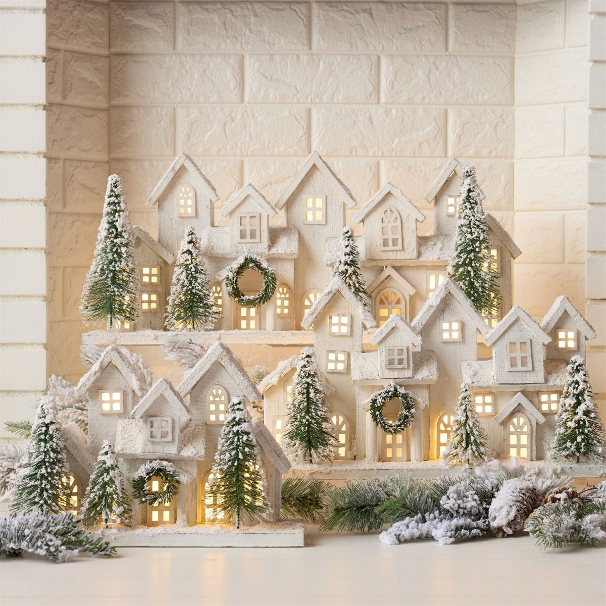 Illuminated white snow-dusted miniature village display with LED-lit houses and bottle brush trees