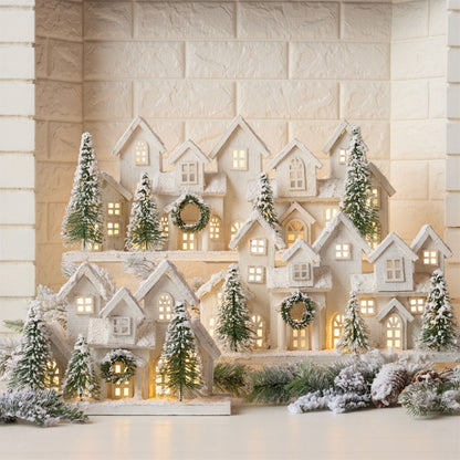 Illuminated white snow-dusted miniature village display with LED-lit houses and bottle brush trees