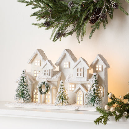 Illuminated white snowy village houses with miniature green trees on a mantel display