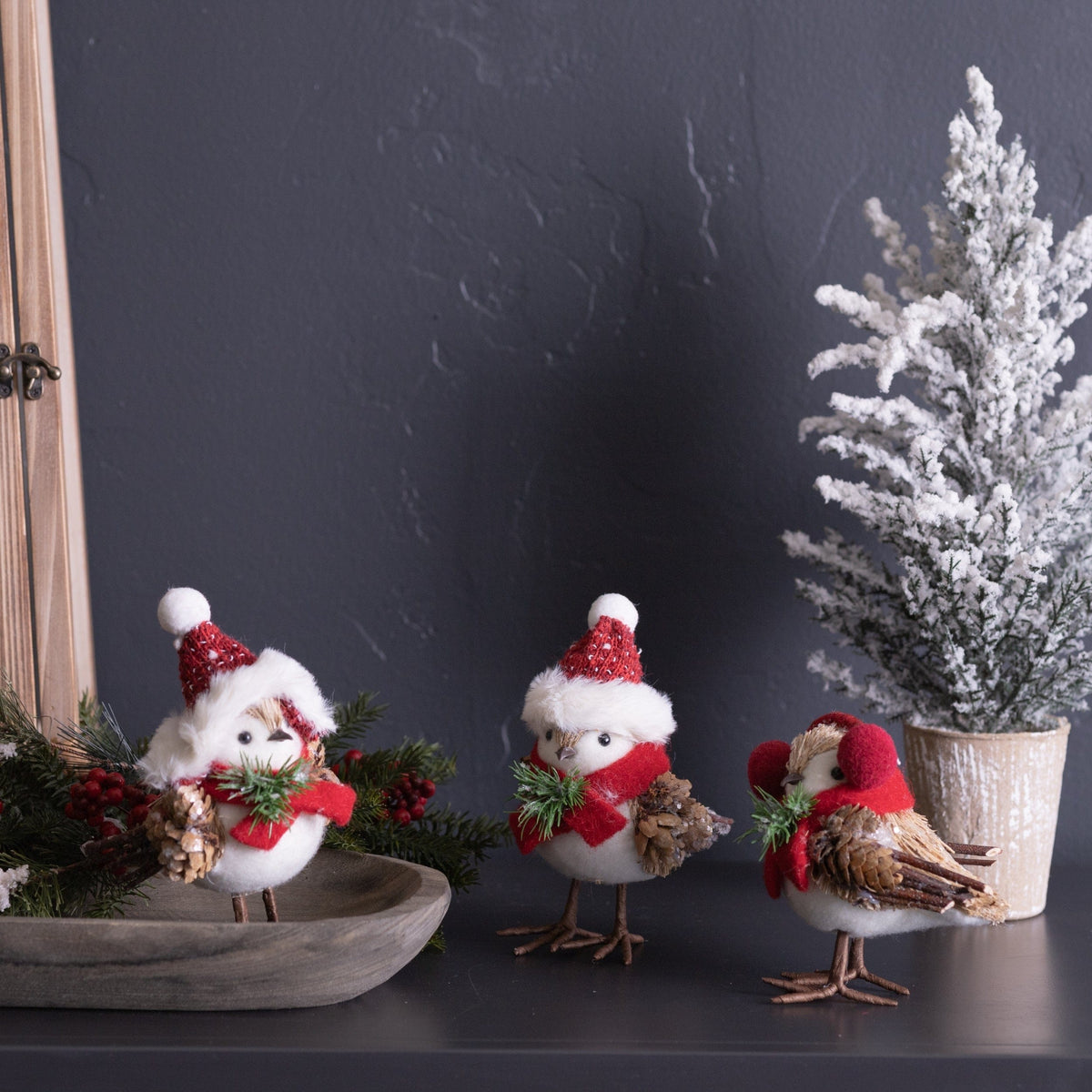 Three decorative holiday birds with white fluffy bodies, red scarves, and Santa hats holding pine cones