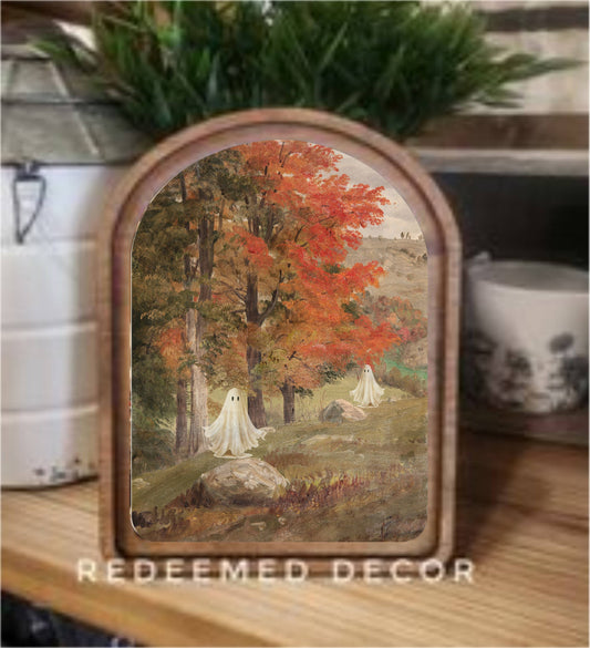Arched wood-framed fall landscape art print with two white ghosts among autumn trees