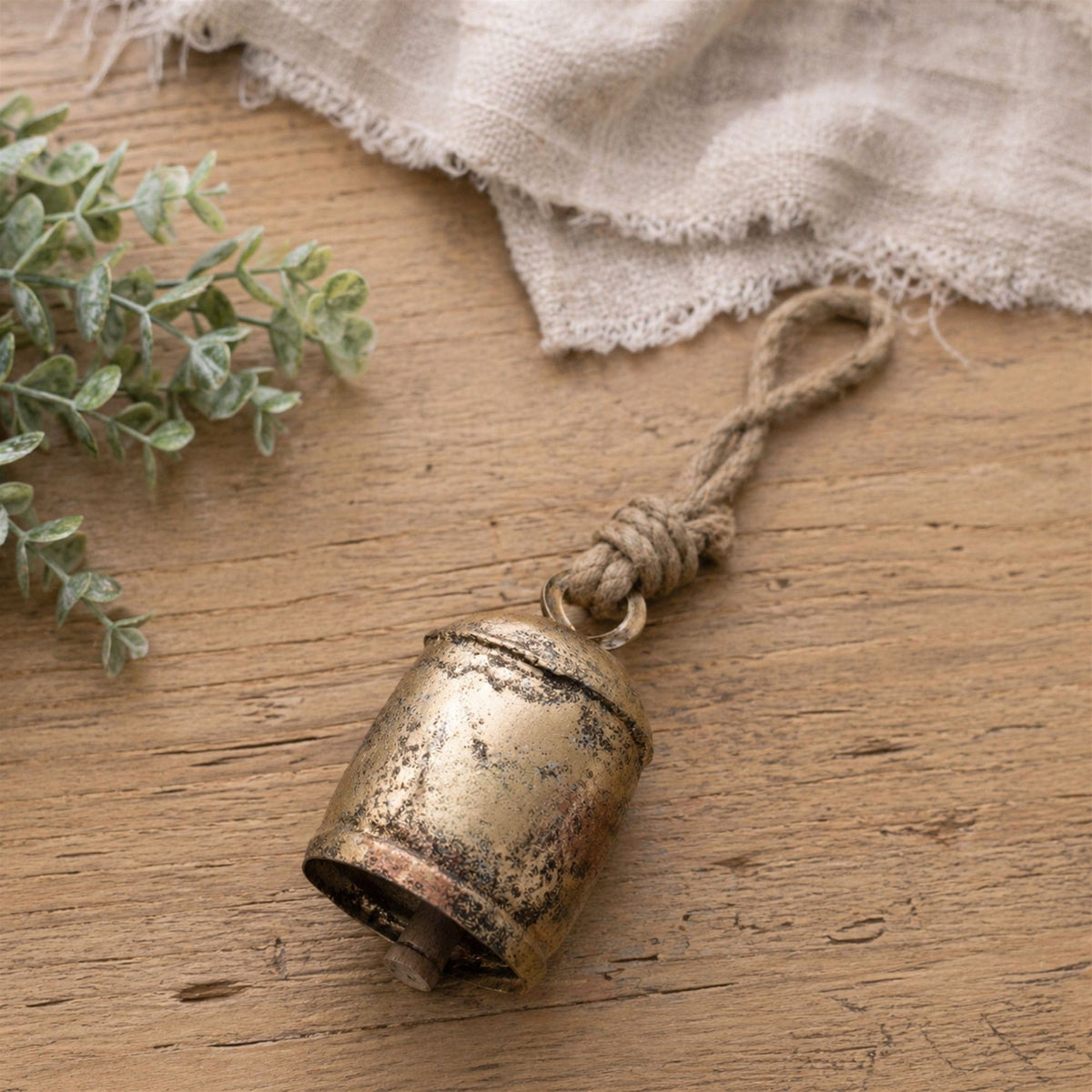 Rustic antique gold iron bell with knotted jute rope hanger, lying on wooden surface