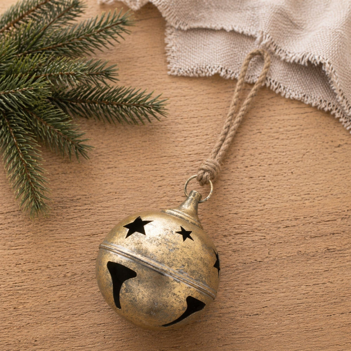 Antique gold jingle bell with star cutouts on a jute cord, beside pine branches