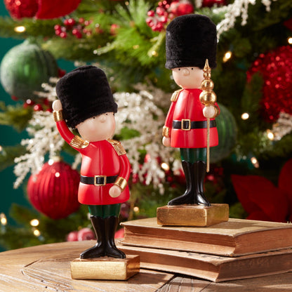 Two toy soldier figurines in red uniforms and black bearskin hats on gold bases