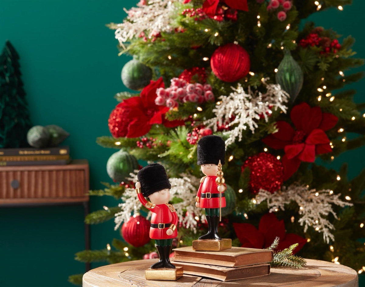 Two decorative toy soldier figurines in red uniforms and black bearskin hats near a Christmas tree