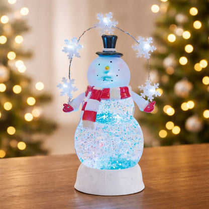 Illuminated snowman snow globe with glitter swirl body, top hat, red scarf, and LED snowflake garland