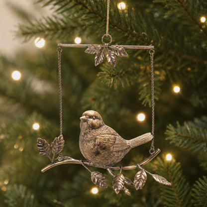 Gold bird figurine perched on decorative metal branch ornament with leaf details, hanging on Christmas tree