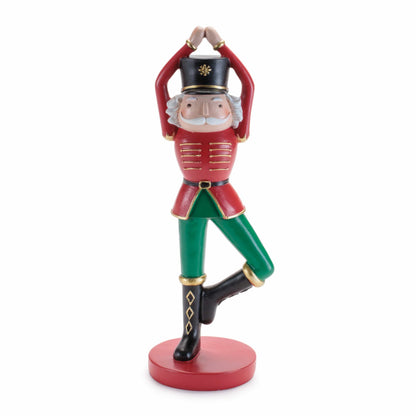 Nutcracker soldier figurine in red jacket and green pants doing yoga tree pose