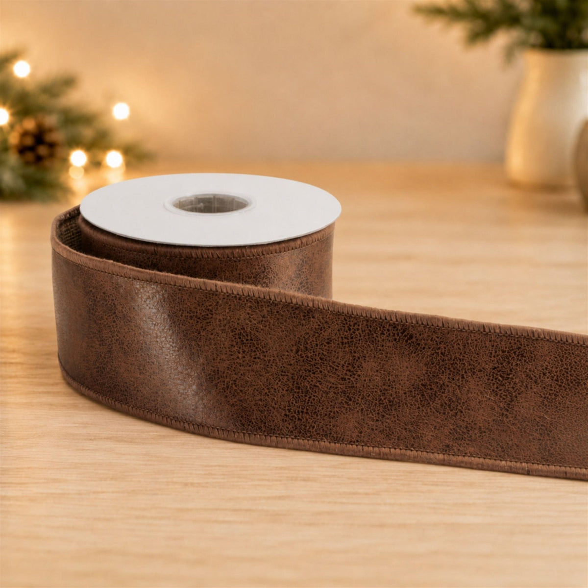 Roll of brown distressed leather-look wired ribbon unrolled on a wooden surface, side view