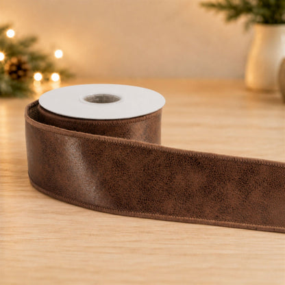 Roll of brown distressed leather-look wired ribbon unrolled on a wooden surface, side view