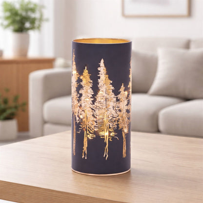 Cylindrical navy luminary with glowing gold cut-out pine tree design on wooden table